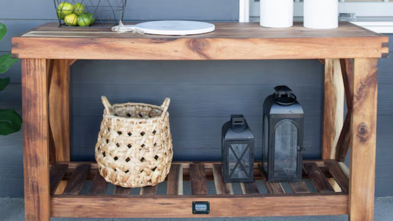 Wooden serving cart with lanterns and wicker basket on shelf.