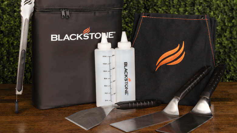 Blackstone griddle toolkit with cooking tools on a wood surface.