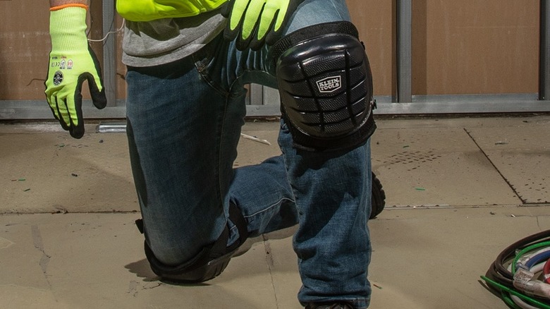 Man in reflective vest kneeling on one knee with Klein Tools knee pads on.