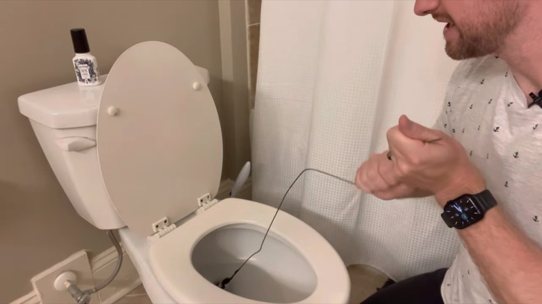 man unclogging toilet with wire hanger