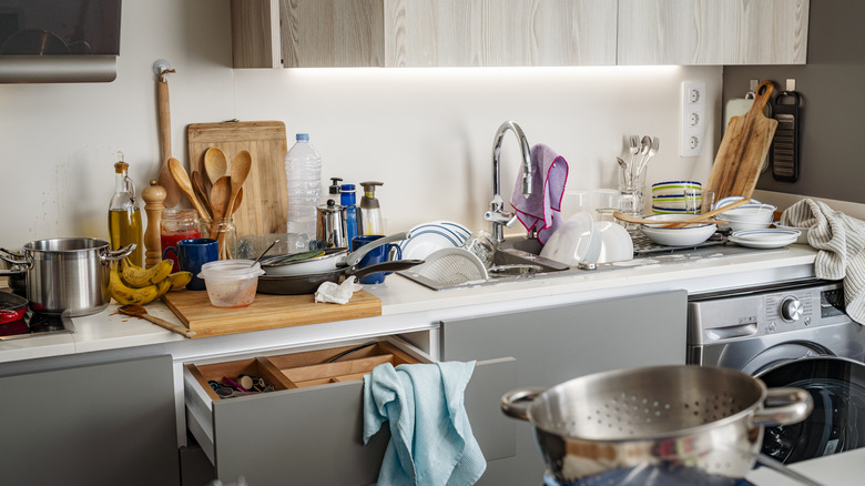 Kitchen counter cluttered with dishes, cutting boards, and cookware.