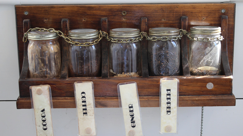 Coffee and spices storied in mason jars on an old wooden wall-mounted shelf.