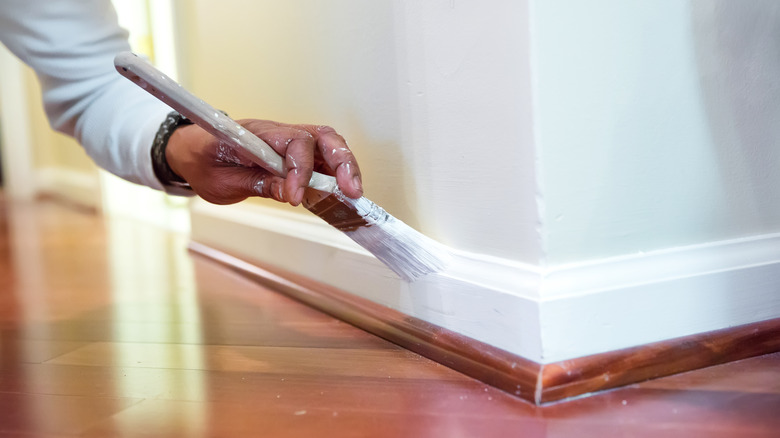Man painting white baseboard 