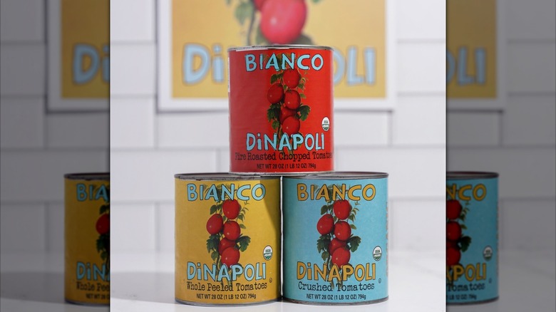 A hand putting pizza sauce on bread in front of a stack of Bianco DiNapoli sauces