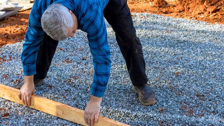 A man leveling small gravel with a wooden beam on top of red soil