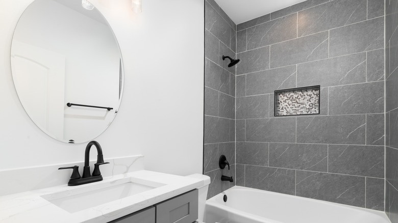 Large format gray tiles in shower above combination bathtub