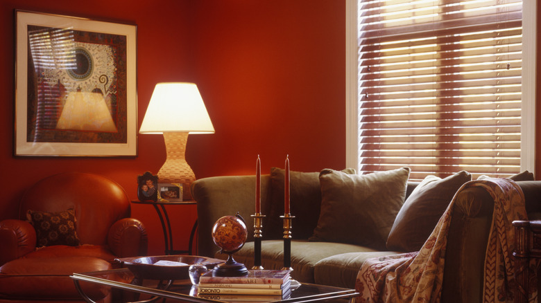 A bright red living room with a brown sofa, soft table lamp, coffee table, and wall art