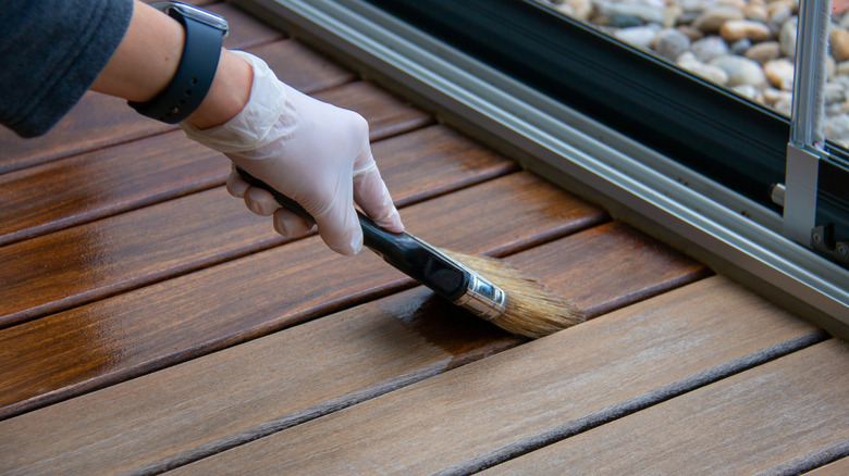 Deck staining, worker applying deck oil on decking boards with paint brush