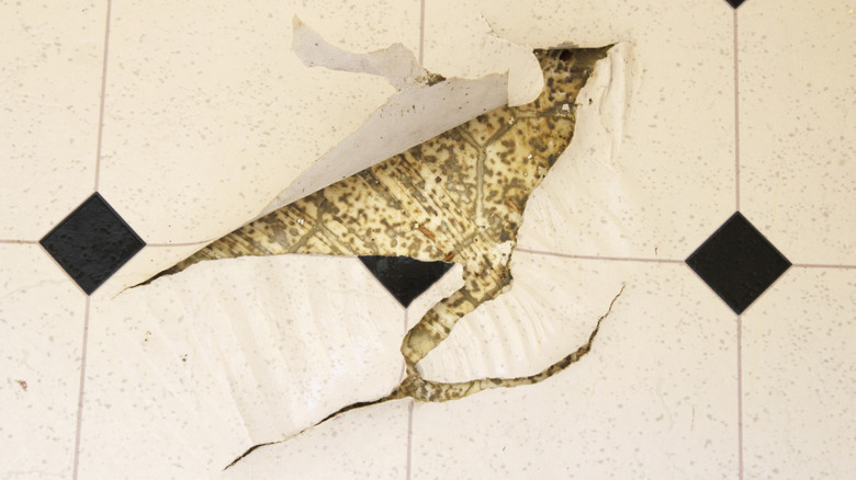 Old white and black speckled linoleum vinyl floor damaged with tears in i