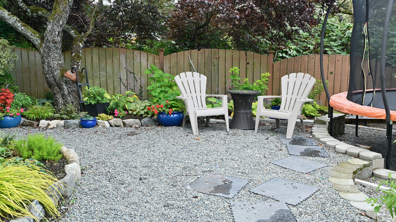 Backyard area covered in gravel with seating and a fence in the background
