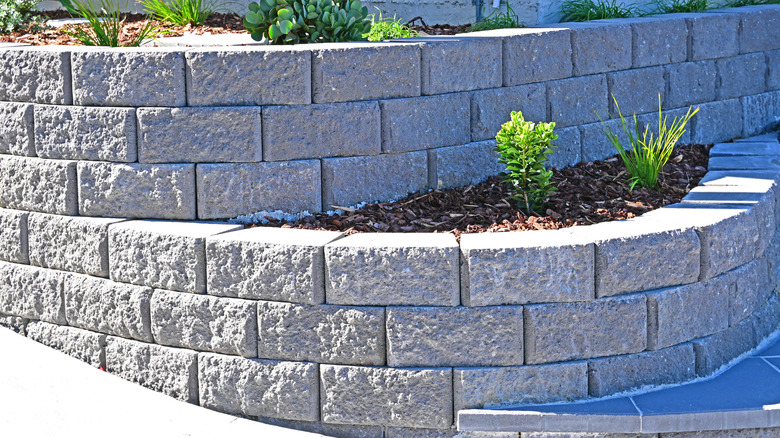 Two-tiered retaining wall made of gray bricks with some greenery