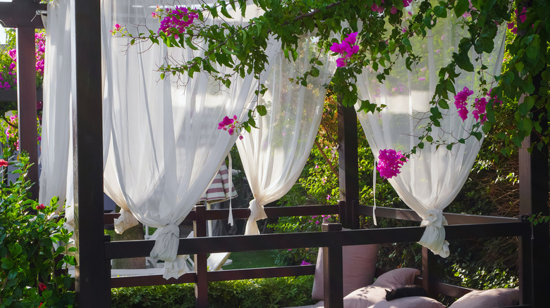 An outdoor sleeping porch with a mattress and white curtains.
