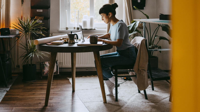A woman working at a desk in a study-slash-parlor room.