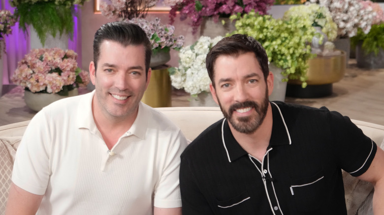 Drew and Jonathan Scott sitting on a couch and smiling.
