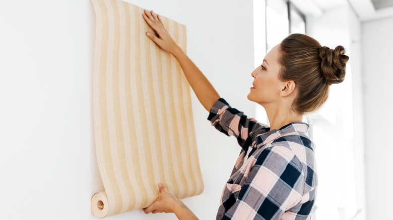 A woman applying vertical striped wallpaper.