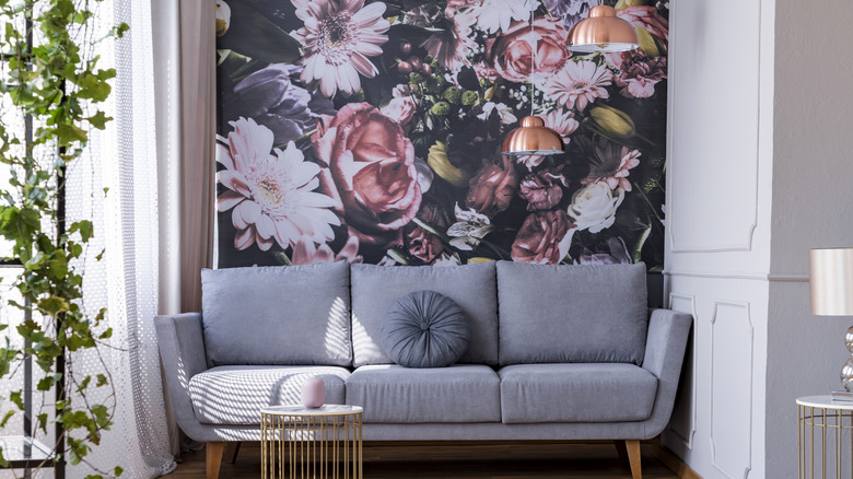 A gray sofa with floral wallpaper behind.