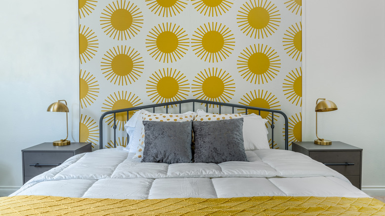 A bed with sun-patterned wallpaper behind the headboard.