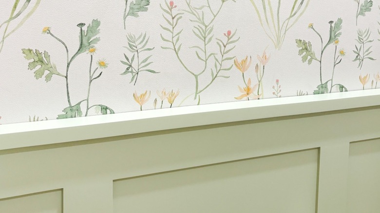 A wall with wainscoting and floral wallpaper.