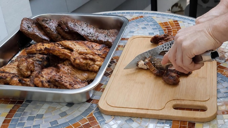 One of Geesta's steel serving trays filled with grilled meat plus a man chopping food on a bamboo cutting board
