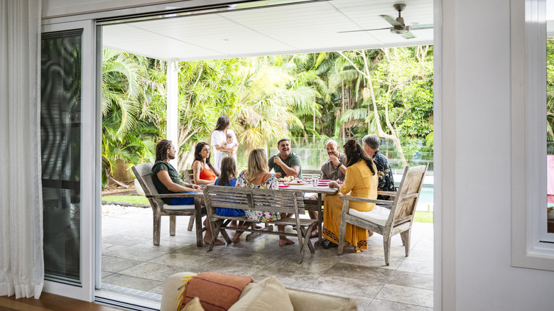 A view from the interior of a house looking out onto the patio where a family is enjoying a meal together