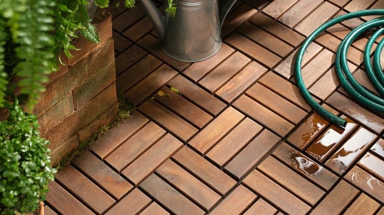 Brown decking tiles near plants with a leaking hose on top