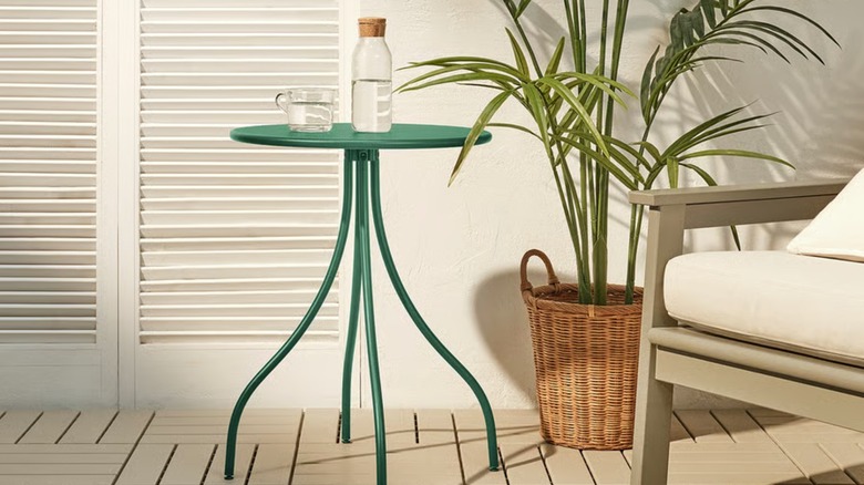 A green side table on a beside a large plant and chair