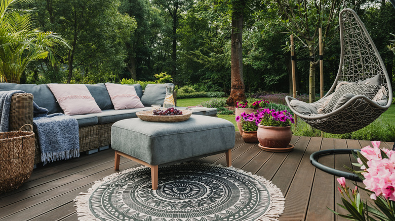 A patio with a rattan sofa covered in blue cushions, a gray and wood ottoman, and a hanging egg chair.