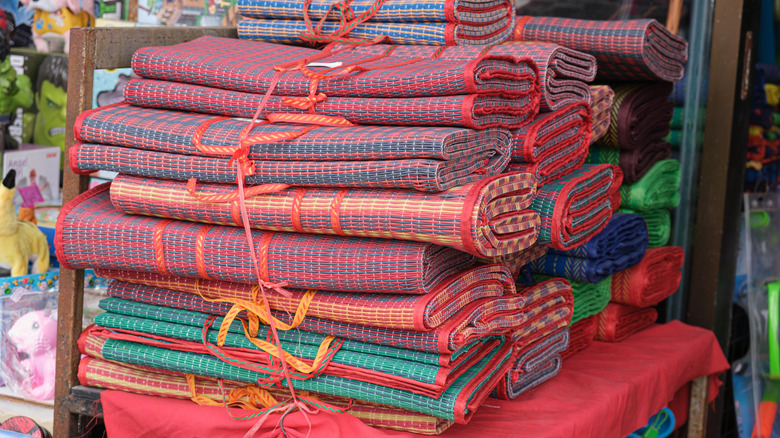 Colorful bamboo beach mats stacked on a chair in a beachside store.