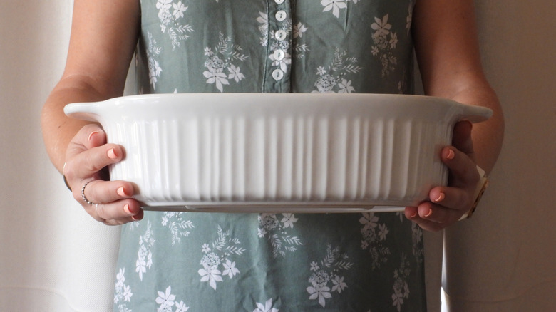 Close up of a person holding a white casserole dish