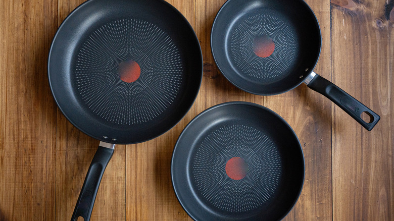 Close up of three frying pans on wooden table
