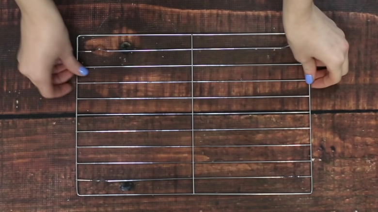 Two hands placing a metal cooling rack on a table.