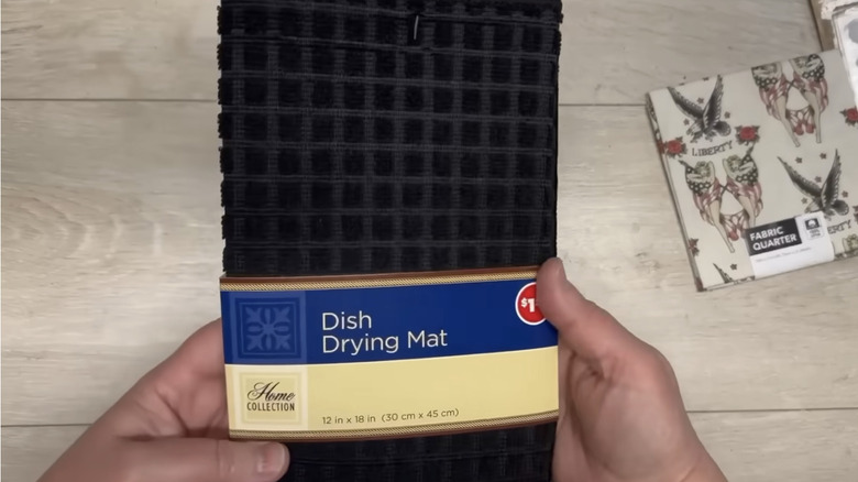 Hand holding up a black dish drying mat.