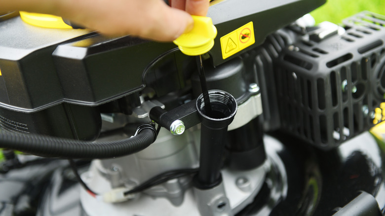 A person checks the oil in a lawnmower