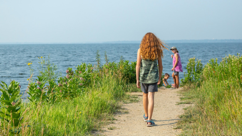 A red-haired girl walks along a lakeshore path with family members in the background.