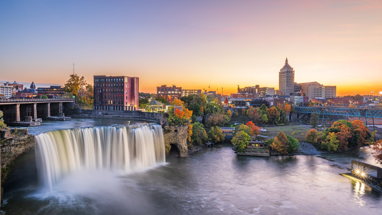 Rochester, New York is viewed at sunset with a waterfall in the foreground.