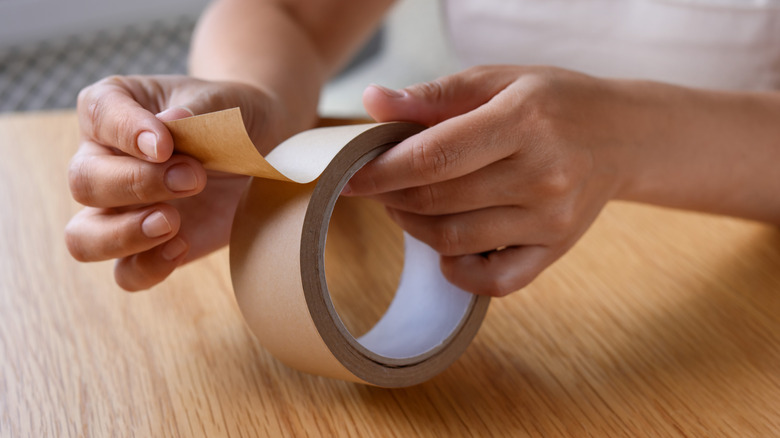 Person at a wooden table holding a roll of masking tape and pulling a piece off