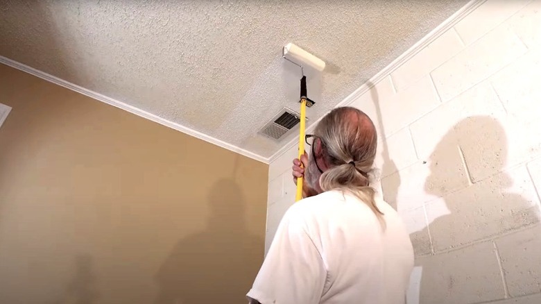 Man painting popcorn ceiling white with extended roller