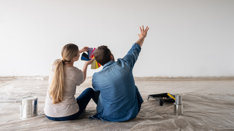 Couple sitting on the floor with paint samples in front of a blank wall