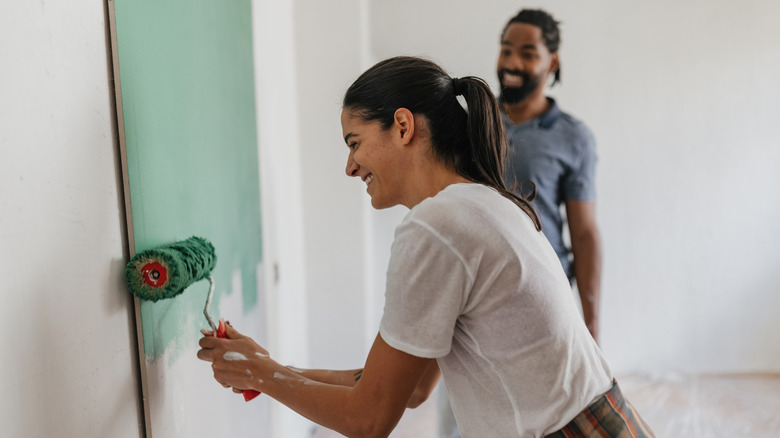 Two people painting a room with green paint with a roller