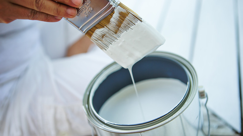 Hand dipping a paint brush into a bucket of blue paint