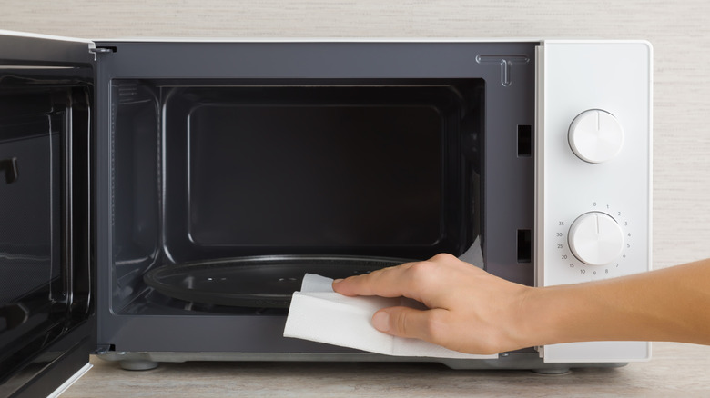 A plain white paper towel is being used along the outer lip of an open microwave.