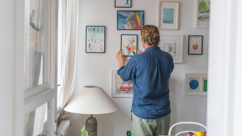 Man hanging small framed print on a collage wall