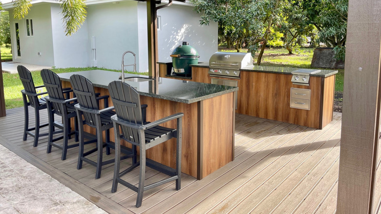 A modern outdoor kitchen with multiple grills, cupboards, and stone countertops.