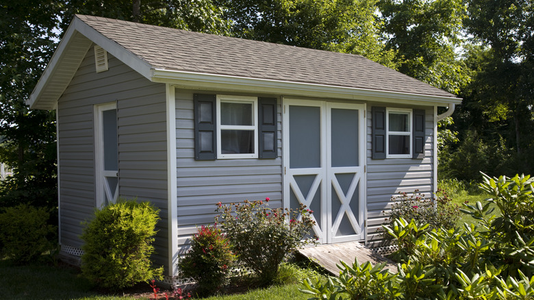 A large shed with windows in a garden setting.