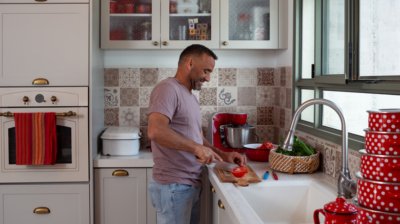 man chopping vegetables in white kitchen with patterned tile backsplash