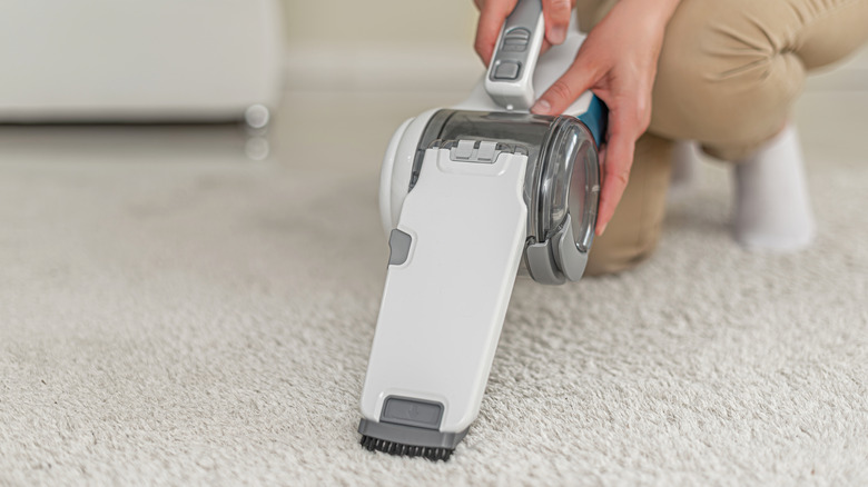 Closeup of a person using a handheld vacuum to spot clean a white carpet