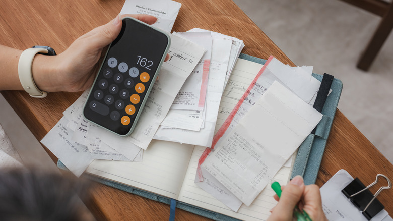 Hand holding a phone with a calculator and receipts on a notebook