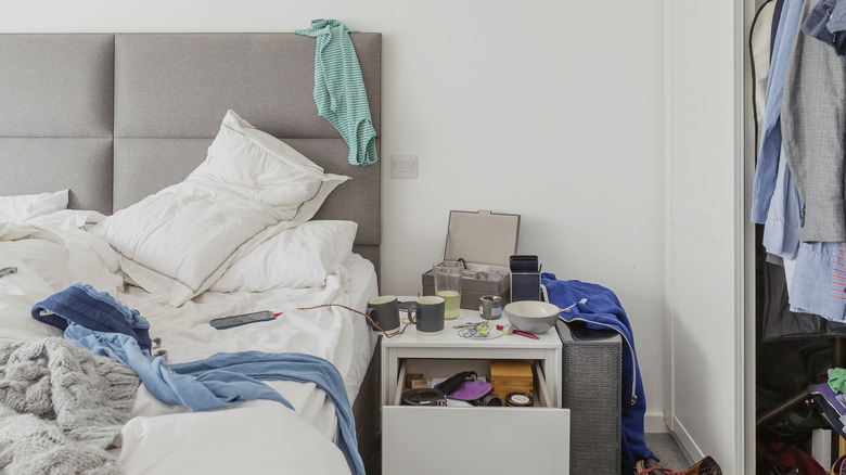A messy bedroom with clutter all over bedside table