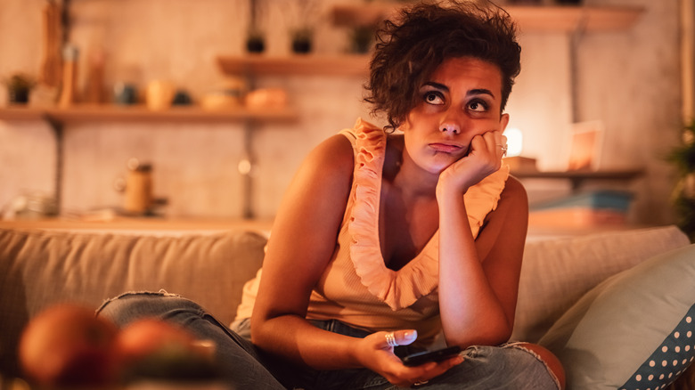 Woman sitting on the couch with a phone in her hand while looking frustrated
