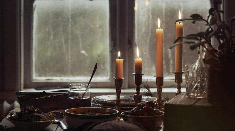 Several taper candles in candle holders burning in front of the window.